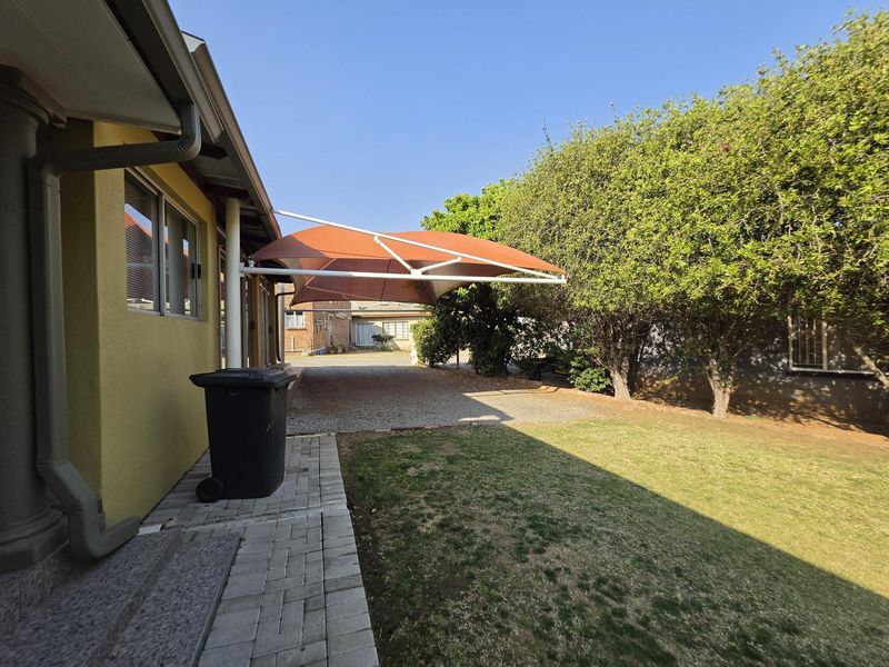 Rear exterior view featuring a gravel driveway, a shade sail structure, and a paved walkway alongside the house.