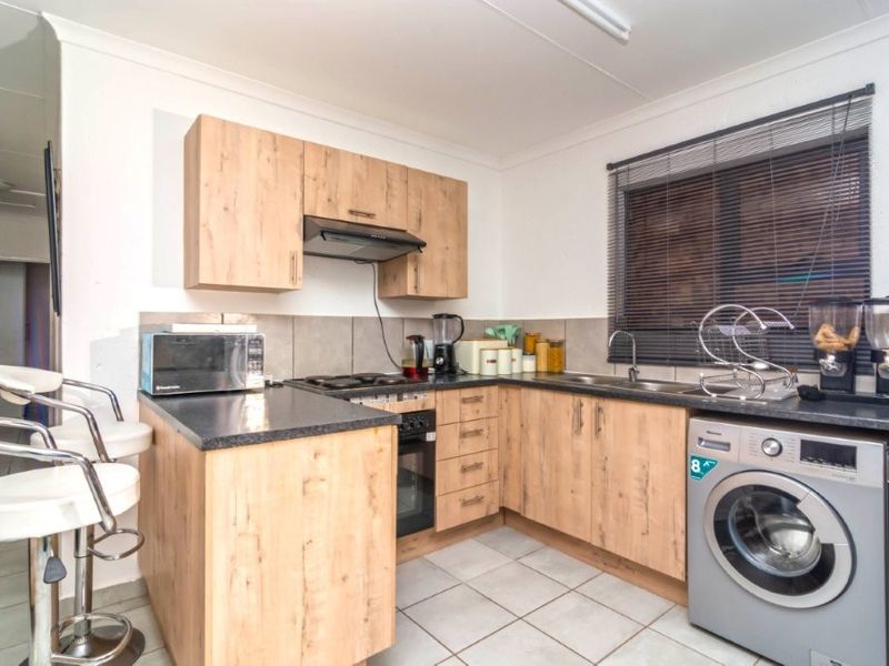 A functional kitchen featuring light wood-look cabinetry, dark countertops, integrated oven and hob, and tiled flooring with a convenient laundry connection.
