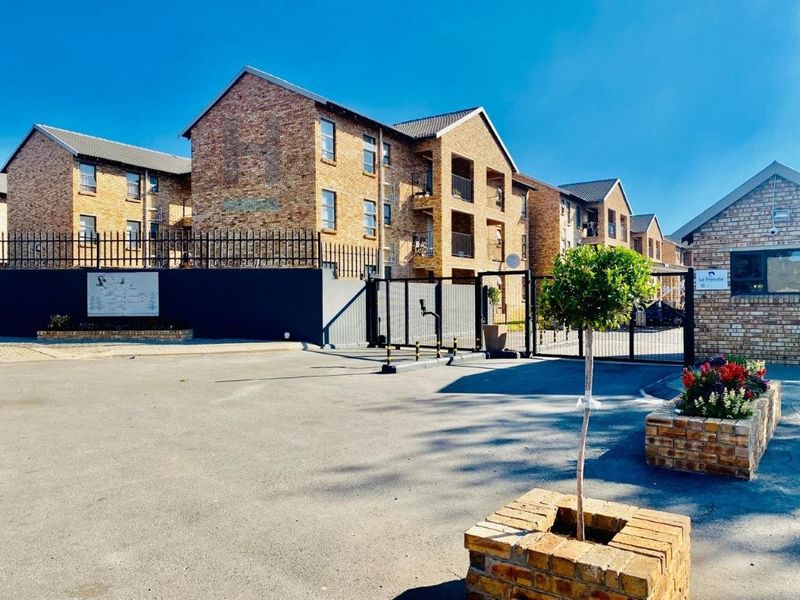 Front entrance view of a multi-story face brick apartment complex featuring secure gated access and paved driveway.
