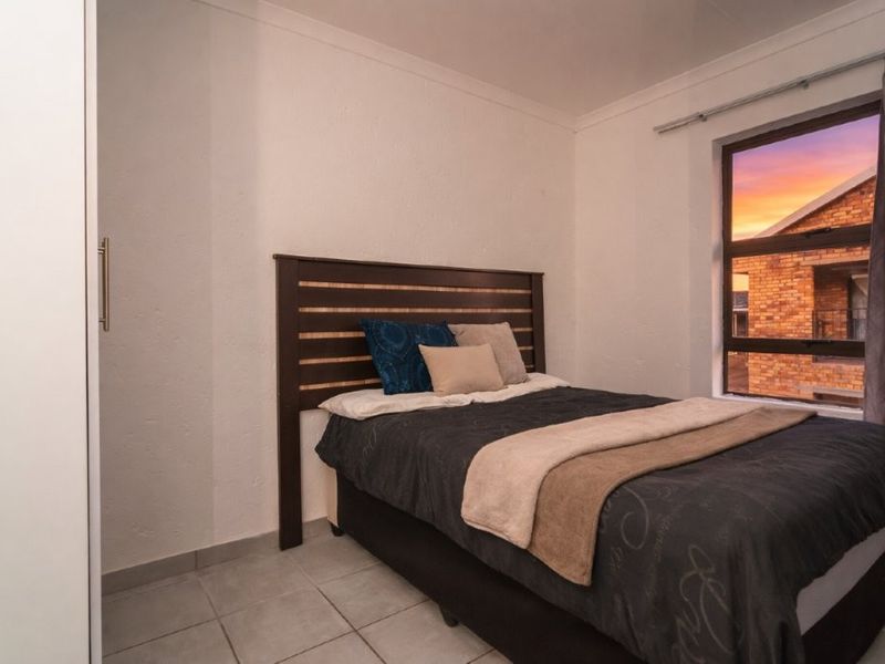 A functional bedroom featuring tiled flooring, a built-in wardrobe, and a window with a view of the surrounding complex.