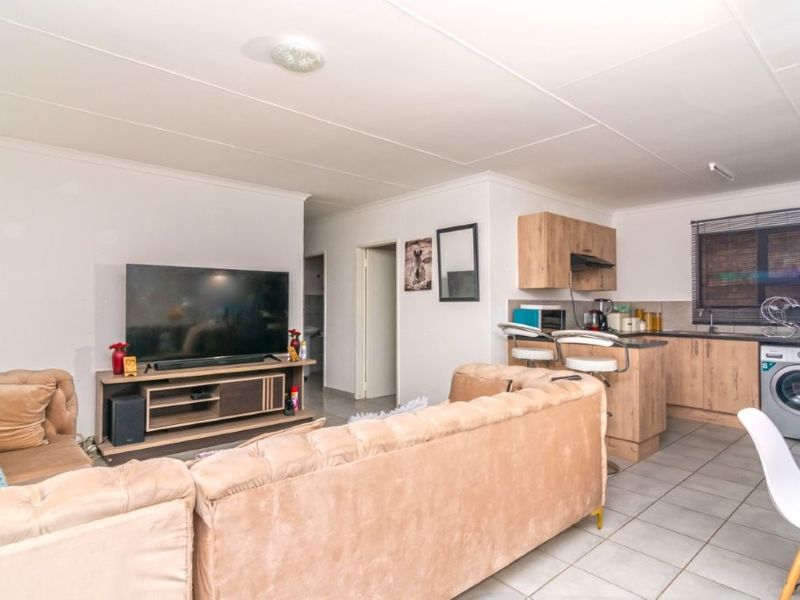 Open-plan living area featuring a functional kitchen with wood-finish cabinetry, tiled flooring, and integrated laundry plumbing, creating a versatile and connected living space.