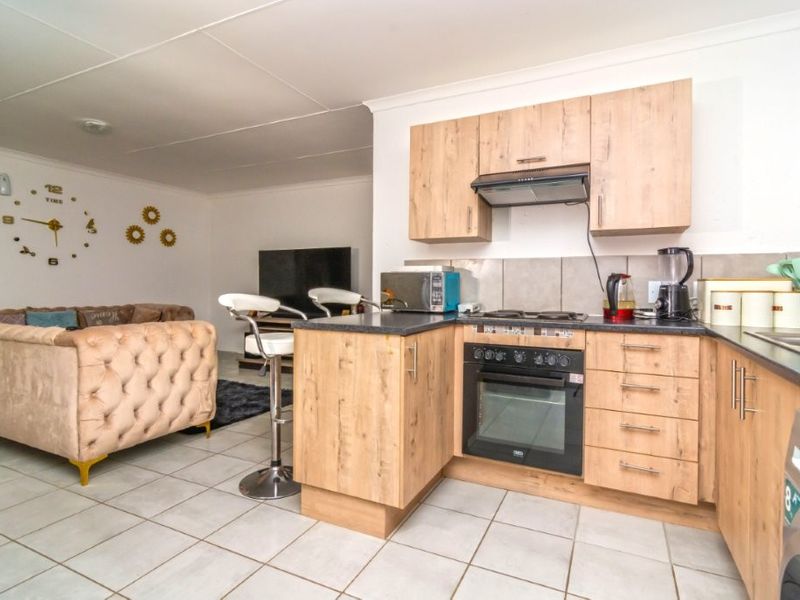 Open plan living area featuring a modern kitchen with wood-finish cabinetry, built-in oven, hob, and tiled flooring, seamlessly connected to the lounge space.