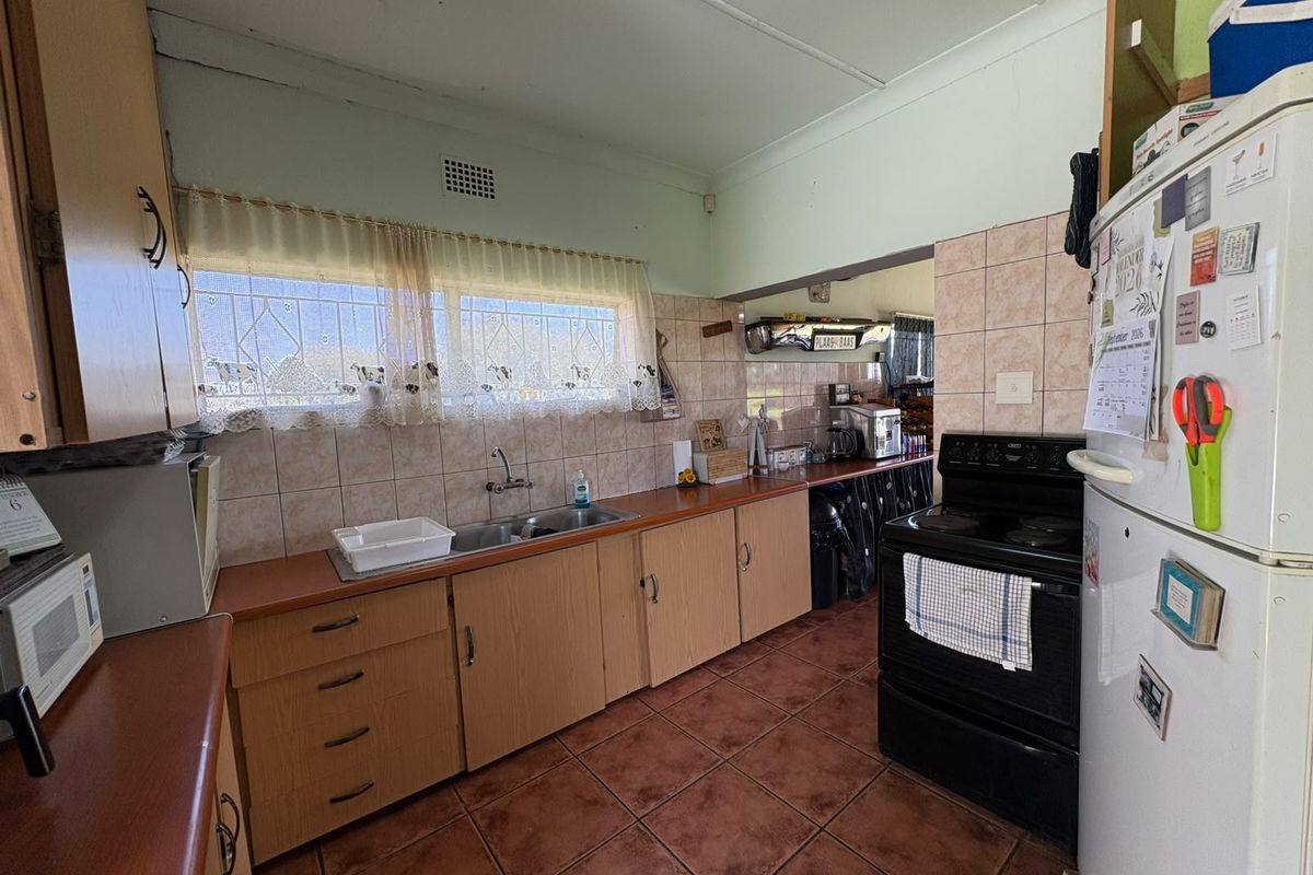 A functional kitchen featuring laminate cabinetry, a double basin sink, tiled backsplash, and ceramic floor tiles, offering potential for modern updates.
