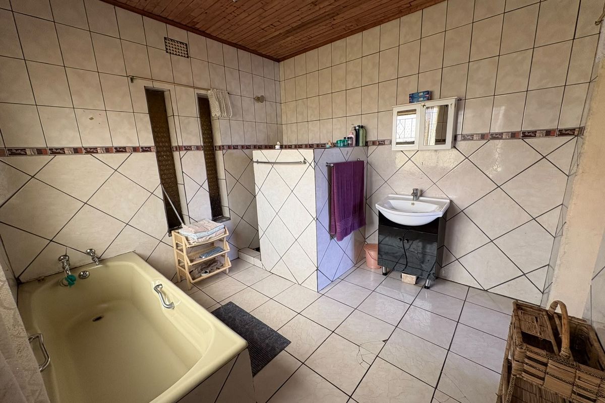 A dated bathroom featuring a built-in bathtub, walk-in shower, and wall-mounted vanity basin, finished with tiled surfaces and a timber ceiling.