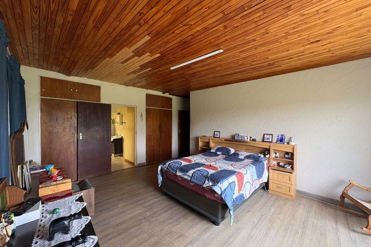Spacious bedroom featuring built-in wooden cupboards, laminate flooring, and a timber-paneled ceiling with visible signs of wear.