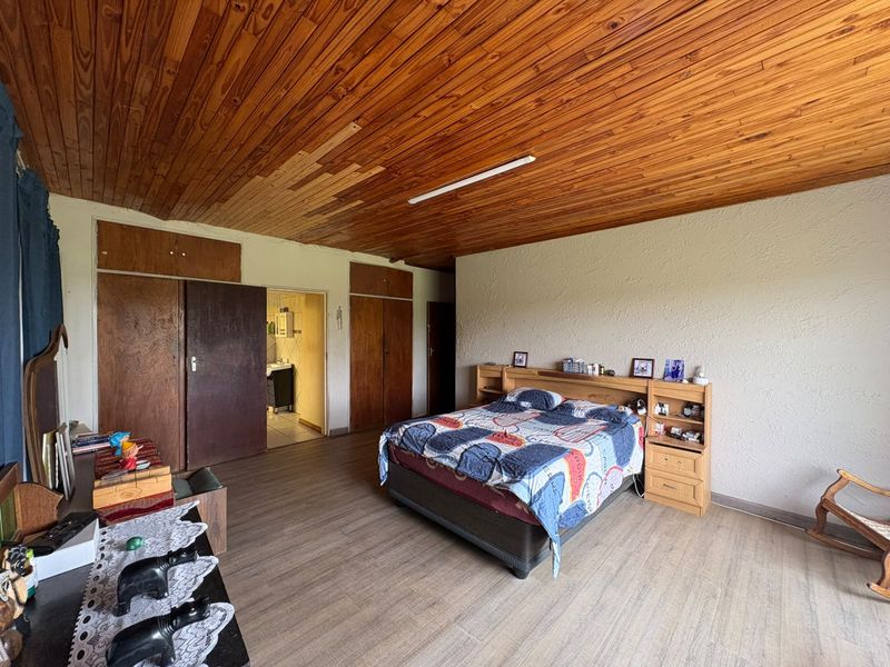 Spacious bedroom featuring built-in wooden cupboards, laminate flooring, and a timber-paneled ceiling with visible signs of wear.