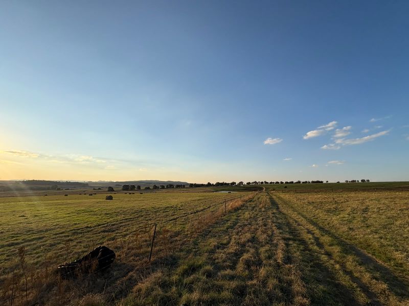 A scenic view of expansive farm pasture land featuring wire fencing and rolling fields under a clear blue sky.