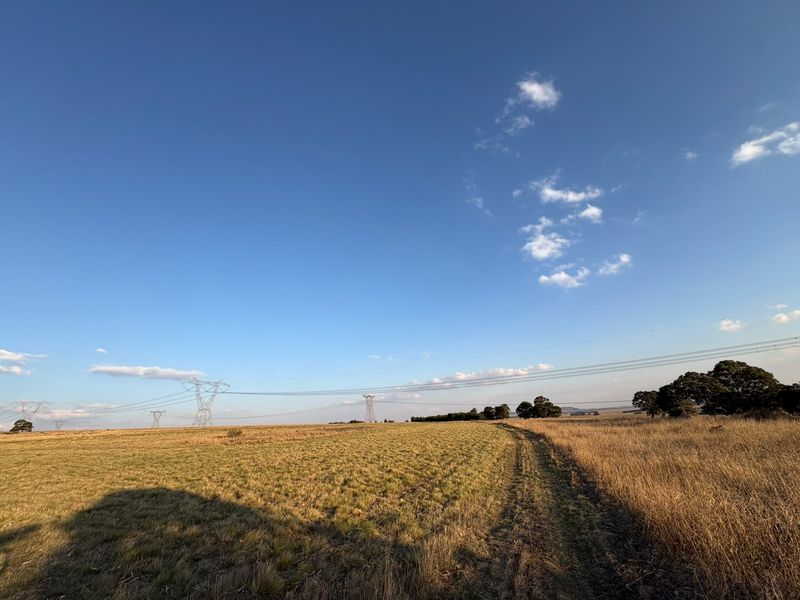 A wide landscape view of open farm fields featuring prominent high voltage electricity pylons and power lines stretching across the horizon.