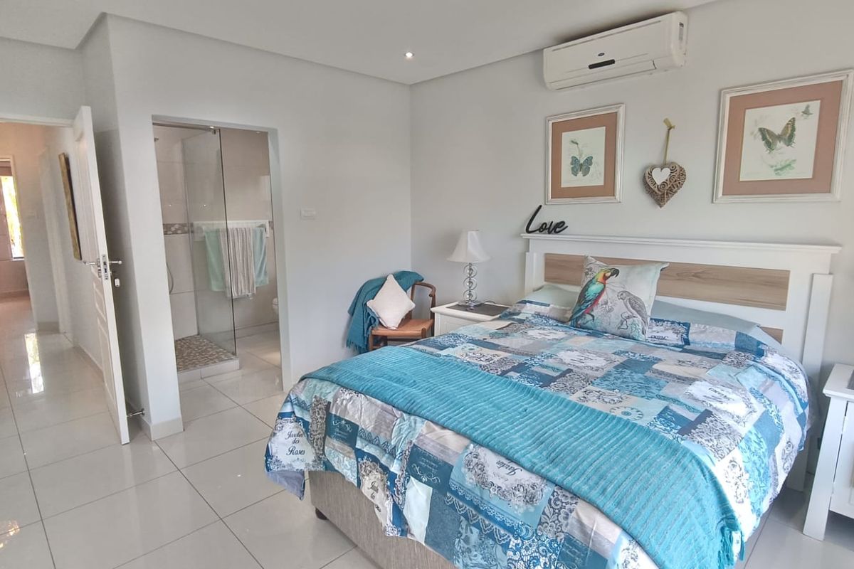 A well-maintained bedroom featuring tiled flooring, recessed lighting, a split-system air conditioner, and an adjoining en-suite bathroom with a glass shower enclosure.