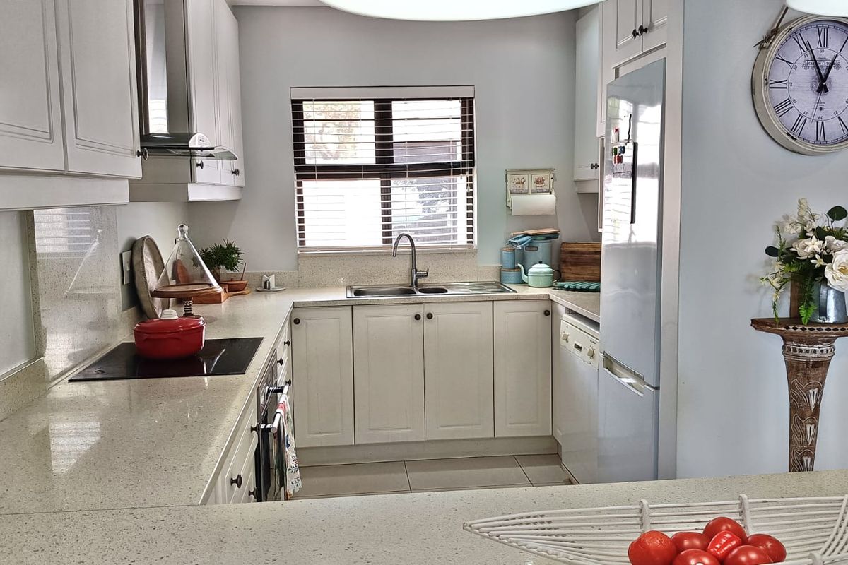 A well-maintained kitchen featuring white cabinetry, stone countertops, integrated appliances, and a functional layout with ample workspace.