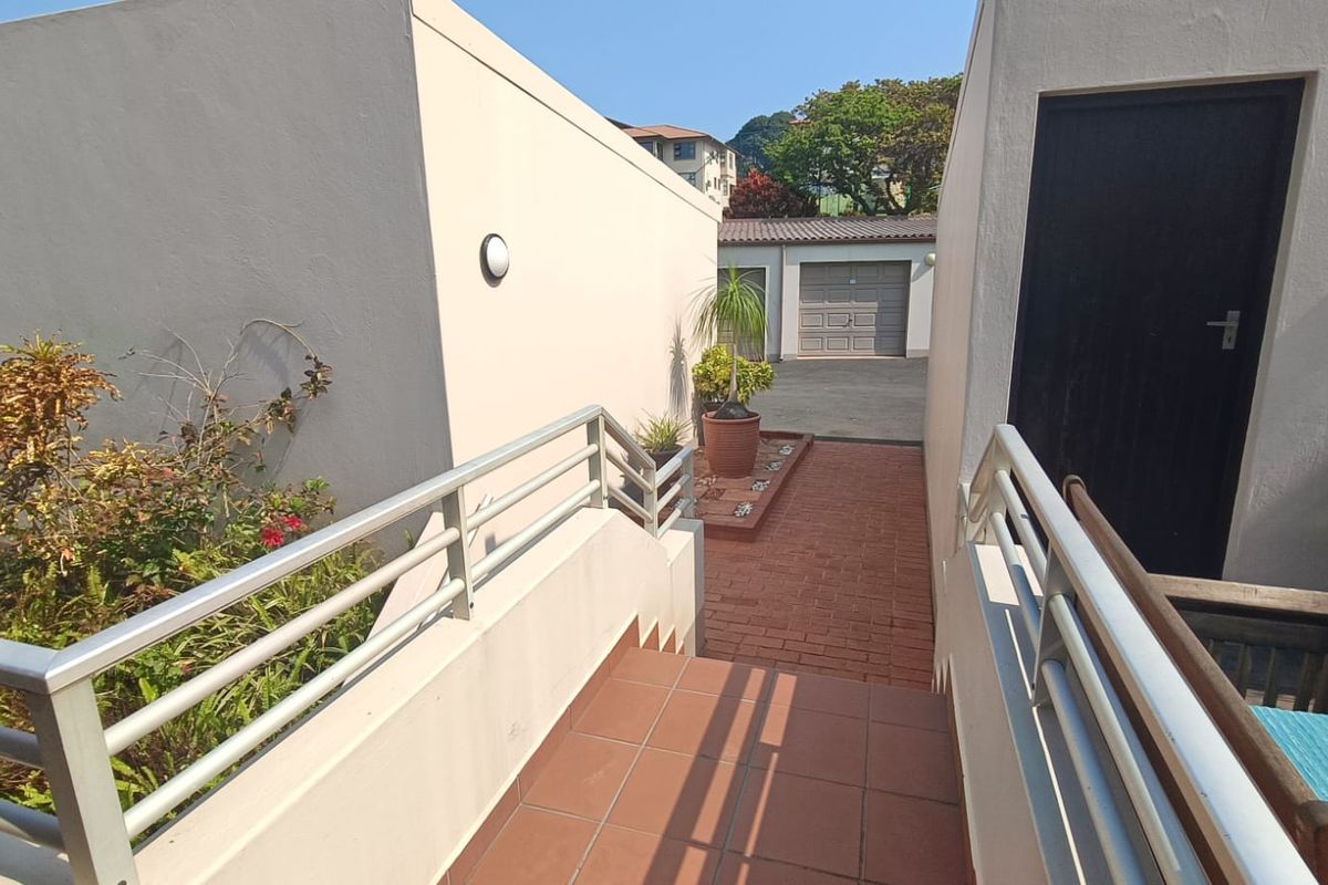 An exterior view showing a tiled staircase with metal handrails leading down to a brick-paved walkway and garage area.