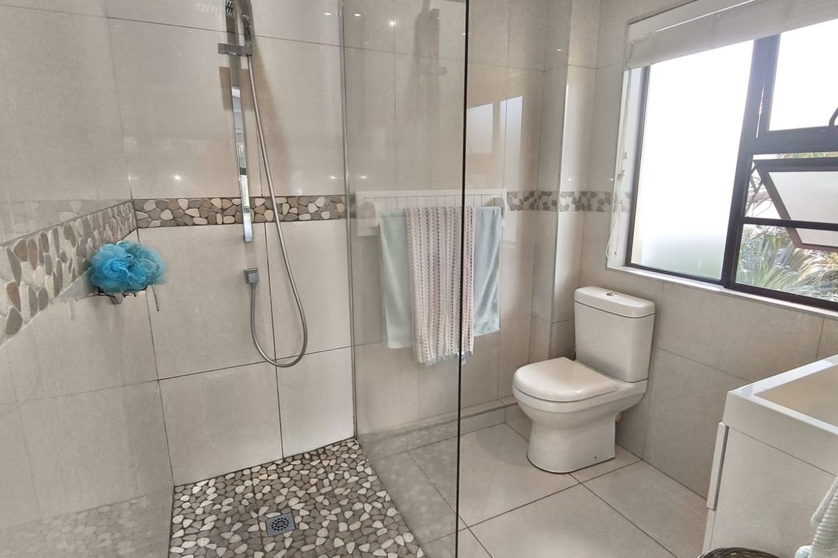 Modern bathroom featuring a walk-in shower with pebble flooring, glass screen, toilet, and vanity basin with neutral wall tiling.