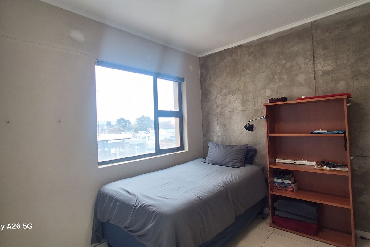 A bedroom featuring an exposed concrete accent wall, tiled flooring, and a large window providing natural light.