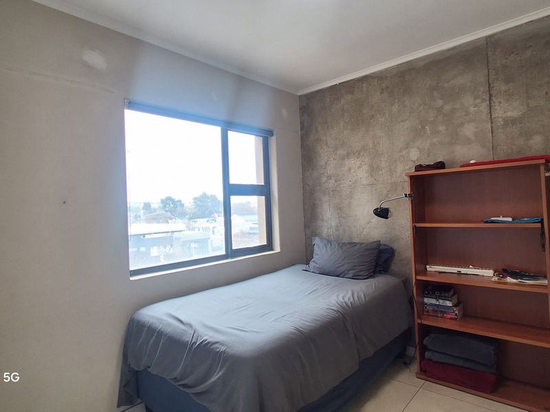 A bedroom featuring an exposed concrete accent wall, tiled flooring, and a large window providing natural light.
