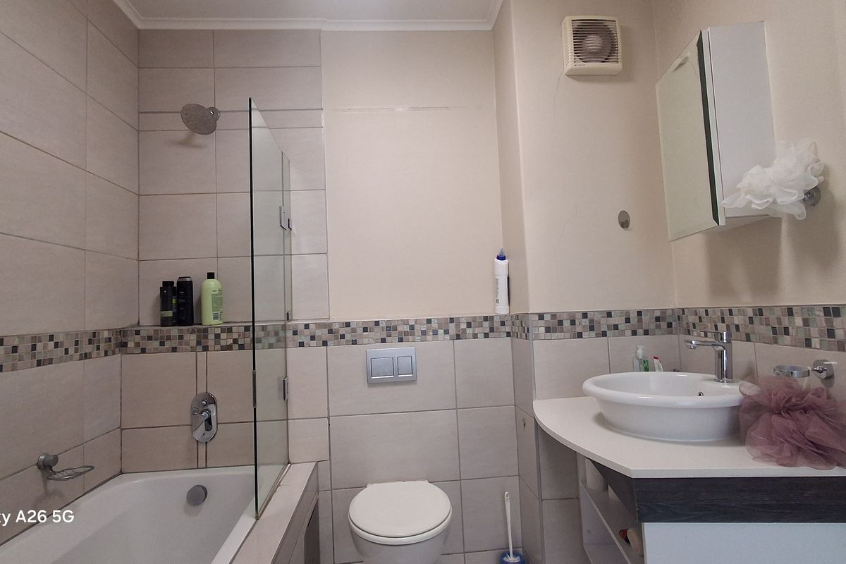 A functional bathroom featuring a bathtub with a glass screen, wall-hung toilet, and a modern vanity basin with tiled finishes.