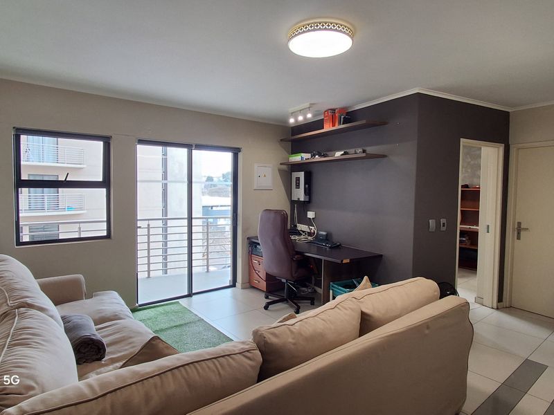 Open plan living area featuring tiled floors, a built-in workspace, and a compact kitchen with subway tile backsplash and sliding door access to a balcony.