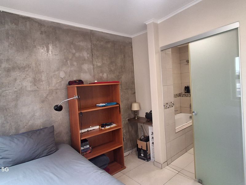 Bedroom featuring a modern concrete accent wall, tiled flooring, and an integrated en-suite bathroom with a sliding frosted glass door.