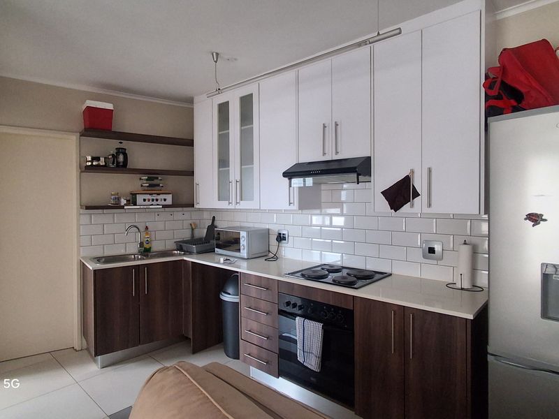 A functional kitchen featuring white upper cabinets, dark wood lower cabinetry, subway tile backsplash, and integrated appliances including an oven and hob.