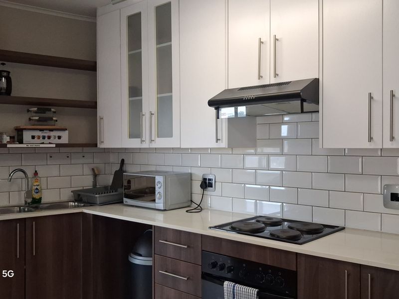 Modern kitchen featuring white cabinetry, subway tile backsplash, quartz countertops, and integrated appliances including an electric hob and oven.