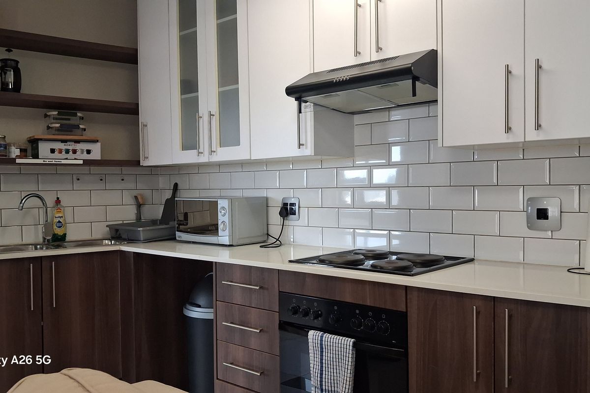 Modern kitchen featuring white subway tile backsplash, quartz countertops, built-in oven with hob, extractor fan, and a mix of white and wood-finish cabinetry.