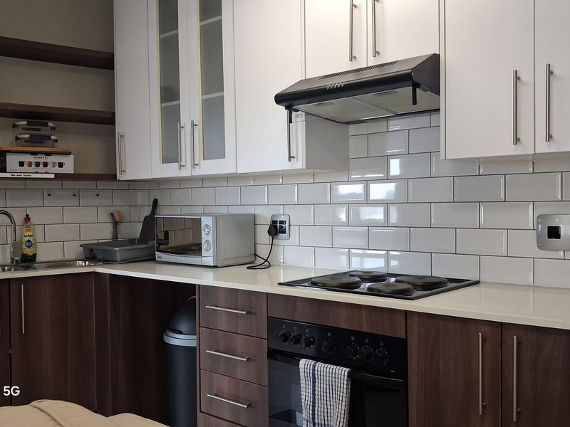 Modern kitchen featuring white subway tile backsplash, quartz countertops, built-in oven with hob, extractor fan, and a mix of white and wood-finish cabinetry.