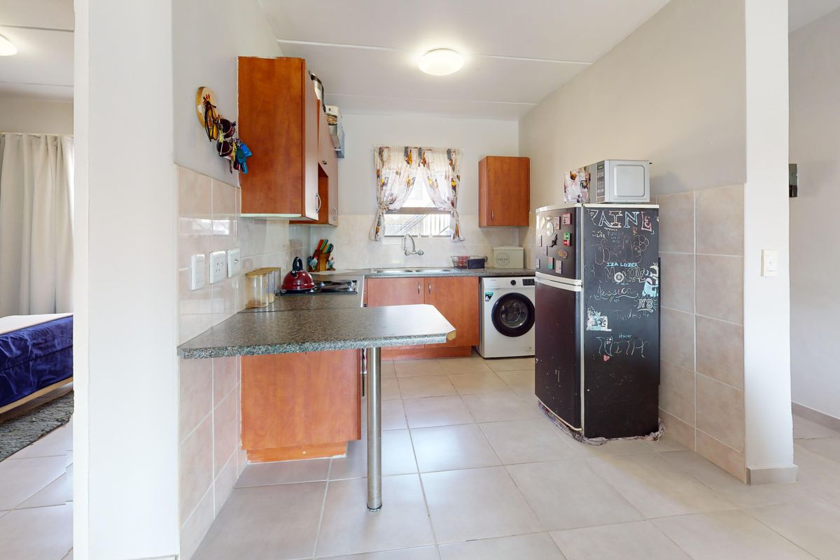 Functional kitchen featuring laminate cabinetry, granite countertops, tiled backsplash, and integrated laundry plumbing, with an attached breakfast bar area.