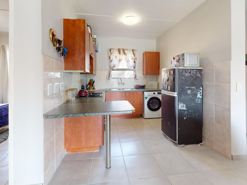 Functional kitchen featuring laminate cabinetry, granite countertops, tiled backsplash, and integrated laundry plumbing, with an attached breakfast bar area.