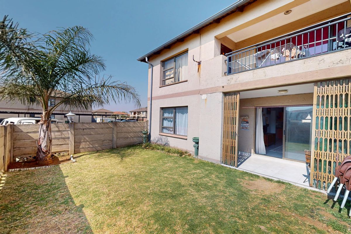 Rear view of the apartment building featuring a private garden, ground floor patio with security gate, and an upper-level balcony.