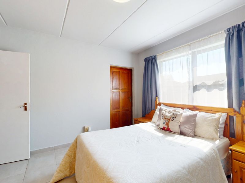 A functional bedroom featuring tiled flooring, a built-in cupboard, and a wooden door, providing a clean and simple living space.