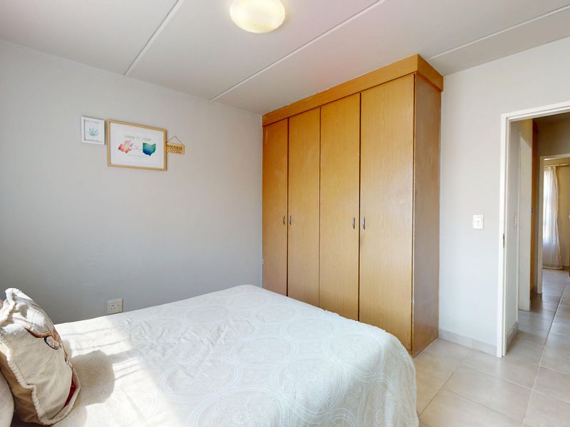 A bedroom featuring neutral walls, tiled flooring, and a large built-in wooden wardrobe, with a doorway leading to an adjacent hallway.