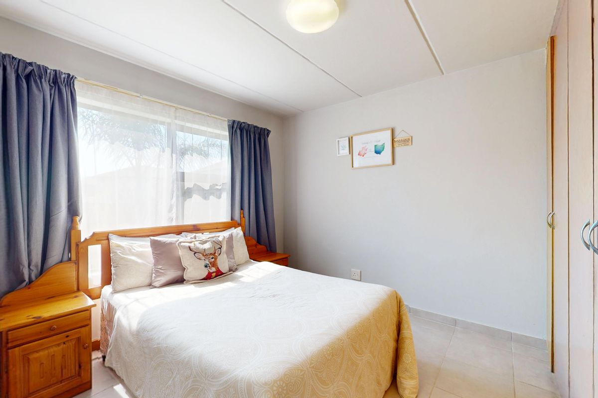 A functional bedroom featuring tiled flooring, a built-in wardrobe, and natural light from a large window.