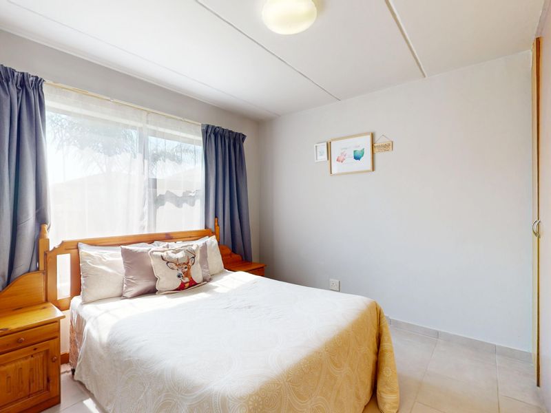 A functional bedroom featuring tiled flooring, a built-in wardrobe, and natural light from a large window.