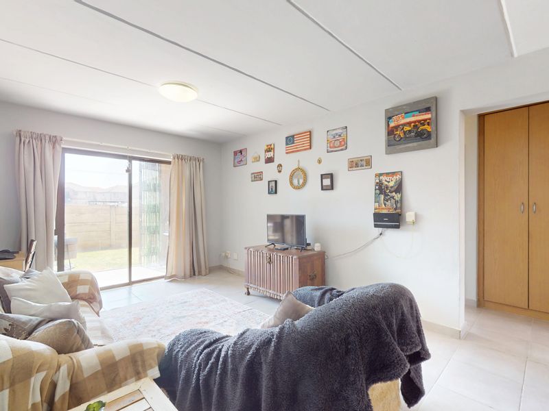 A bright living room featuring tiled flooring, a sliding glass door leading to the exterior, and a built-in storage cupboard.