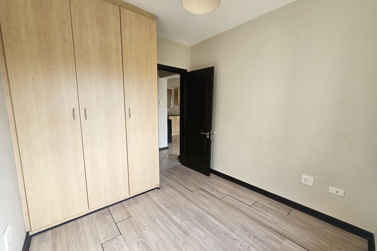 A vacant bedroom featuring light wood-look laminate flooring, a large built-in wardrobe, and neutral wall finishes.