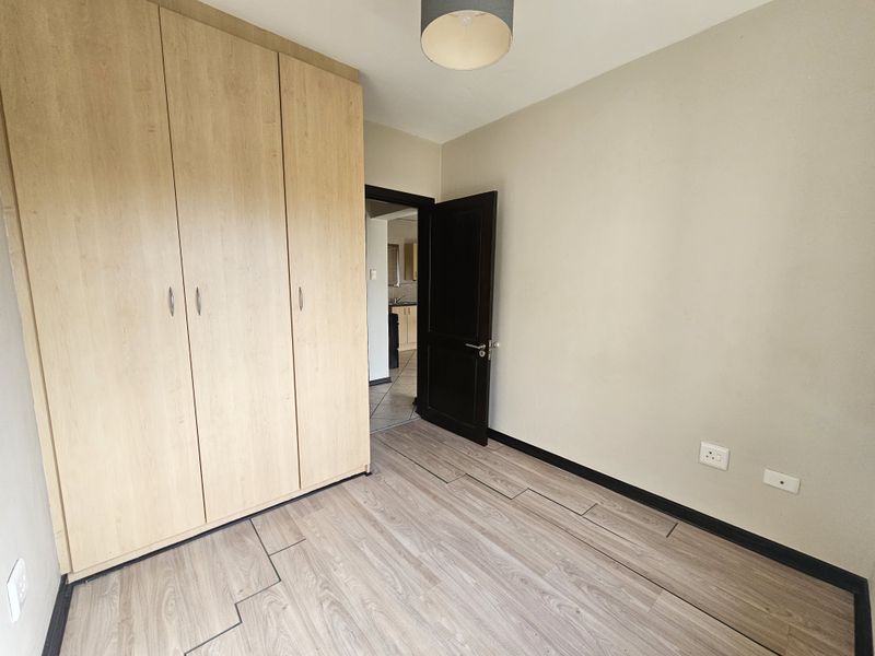 A vacant bedroom featuring light wood-look laminate flooring, a large built-in wardrobe, and neutral wall finishes.