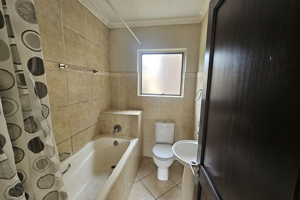 A compact bathroom featuring a bathtub, pedestal sink, and toilet with neutral wall and floor tiling, requiring some maintenance and cosmetic updates.