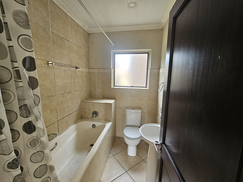A compact bathroom featuring a bathtub, pedestal sink, and toilet with neutral wall and floor tiling, requiring some maintenance and cosmetic updates.