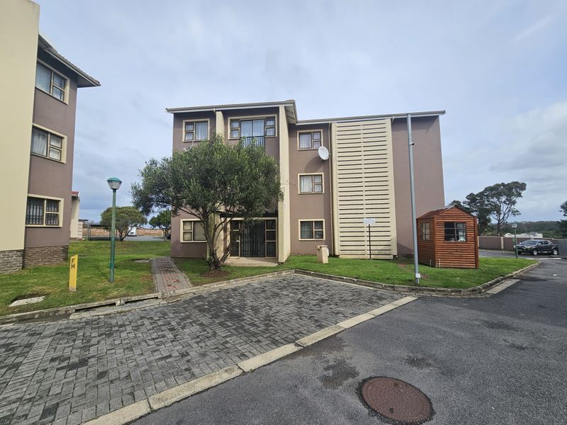 Exterior view of a multi-story apartment building featuring paved parking, landscaped grounds, and a security-gated entrance.