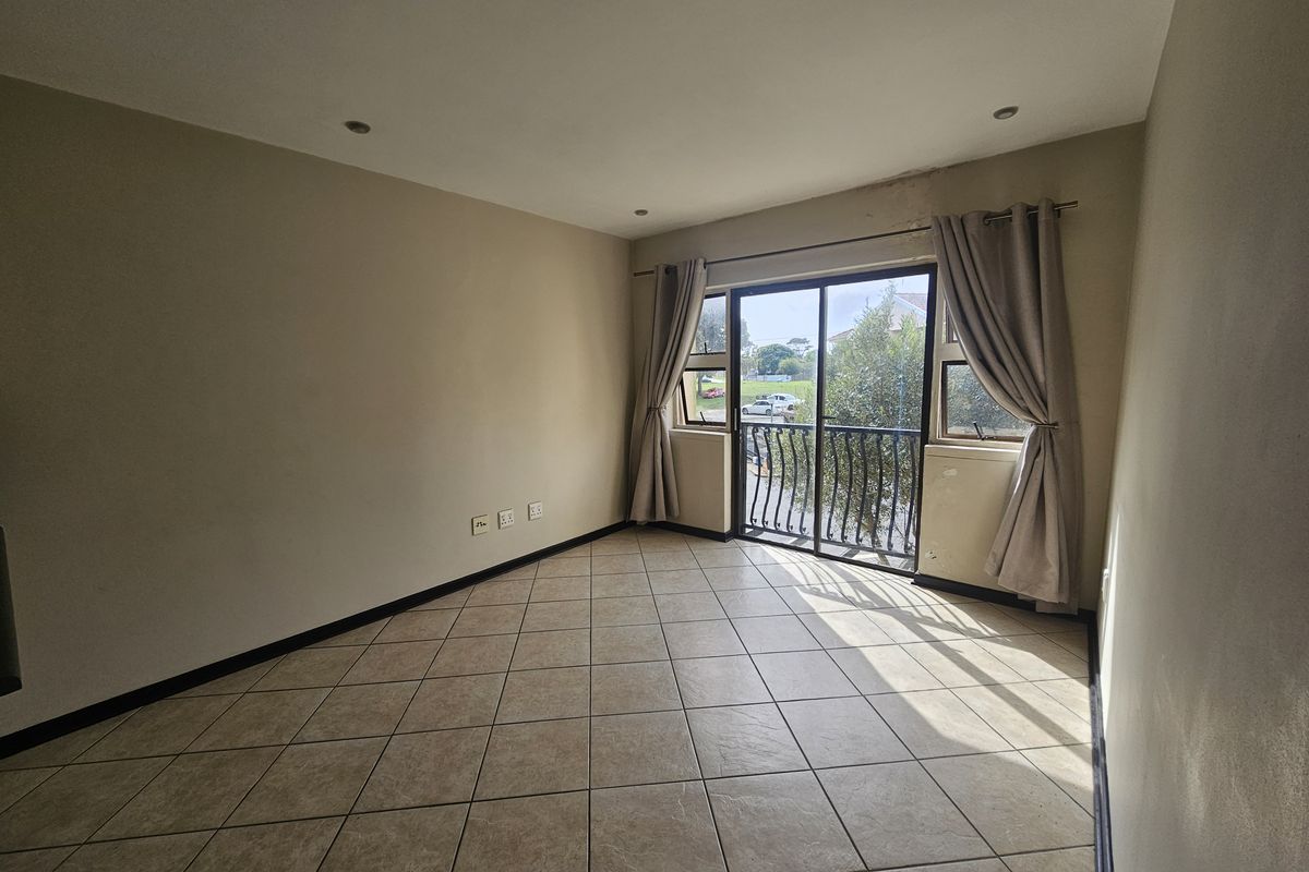 An empty living room featuring tiled floors, recessed lighting, and a sliding glass door leading to a small balcony with a metal railing.