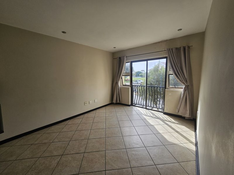 An empty living room featuring tiled floors, recessed lighting, and a sliding glass door leading to a small balcony with a metal railing.