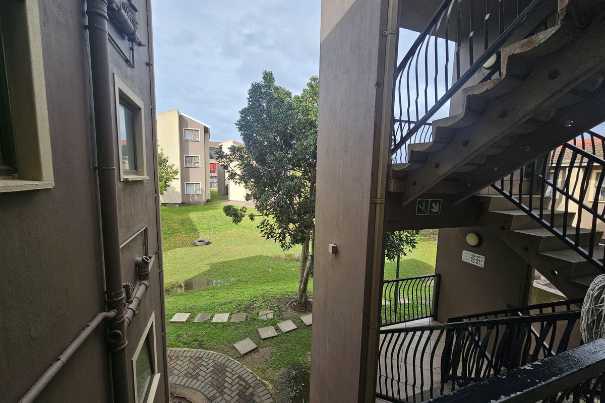 View of the apartment complex exterior featuring a concrete staircase, metal balustrades, and access to a communal garden area.