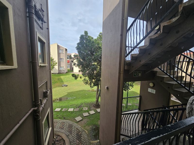 View of the apartment complex exterior featuring a concrete staircase, metal balustrades, and access to a communal garden area.