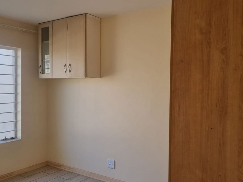An empty bedroom featuring tiled flooring, a built-in wall cabinet, and a window fitted with security bars.