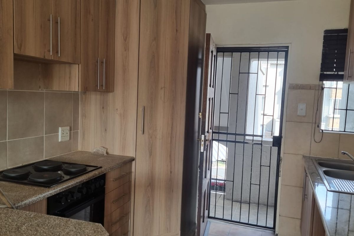 A functional kitchen featuring wood-look cabinetry, granite countertops, an integrated electric hob and oven, and a double sink with a tiled backsplash.
