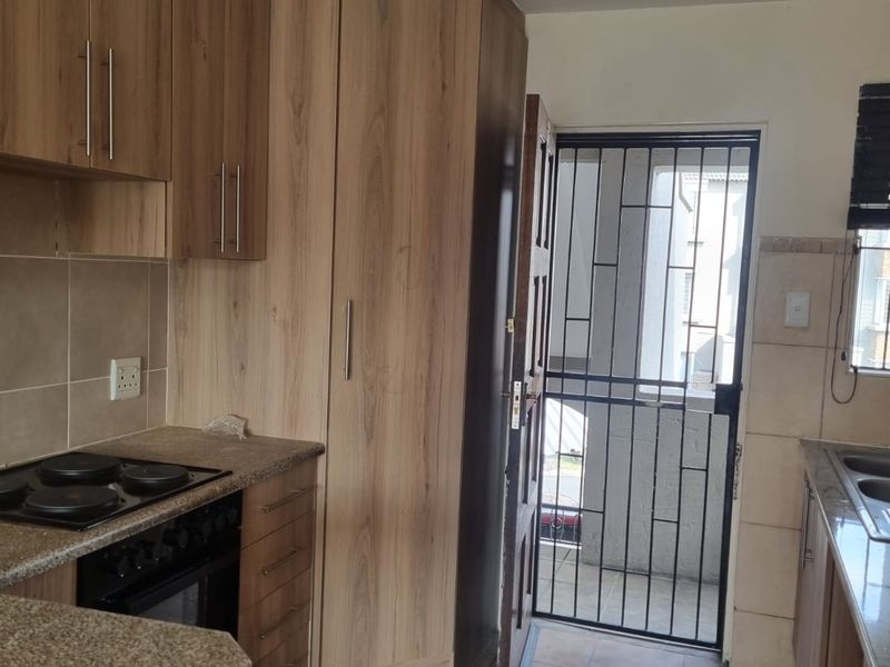 A functional kitchen featuring wood-look cabinetry, granite countertops, an integrated electric hob and oven, and a double sink with a tiled backsplash.