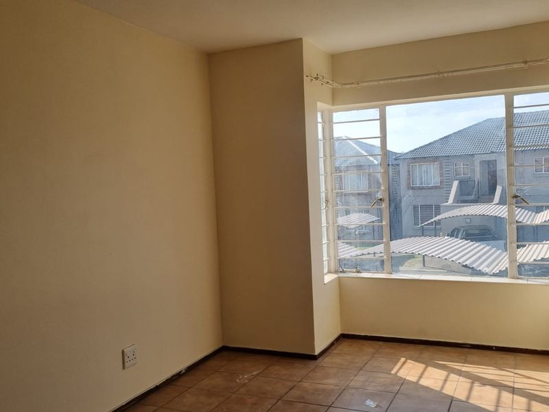 An empty bedroom featuring tiled flooring and a large bay window that provides natural light and views of the surrounding complex.