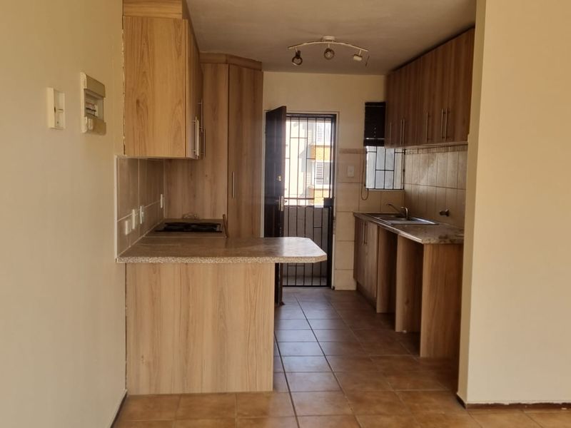 A functional kitchen featuring laminate cabinetry, stone countertops, a built-in hob, and tiled flooring, with direct access to an exterior security gate.