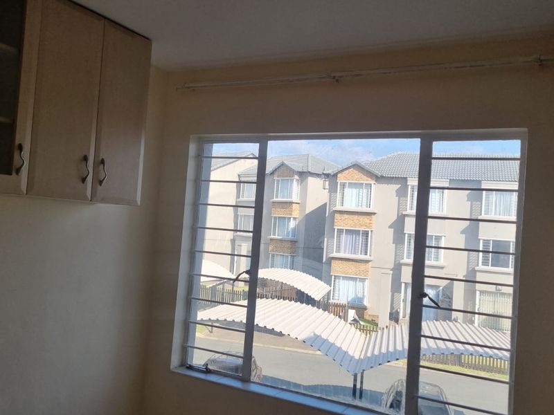 A bright, empty bedroom featuring built-in wall cabinetry and large windows with security bars, offering a view of the surrounding residential complex.
