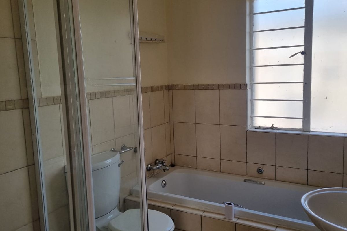 A functional bathroom featuring a shower enclosure, bathtub, toilet, and washbasin with tiled finishes and a window with security bars.