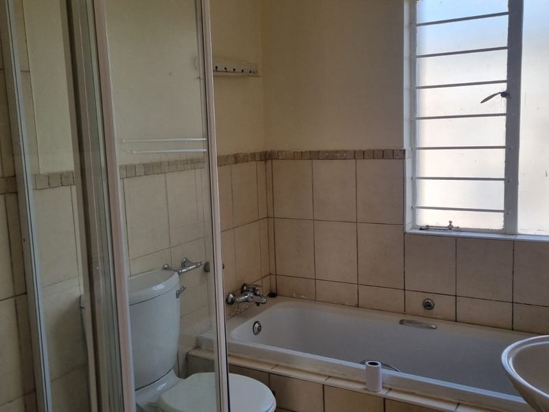 A functional bathroom featuring a shower enclosure, bathtub, toilet, and washbasin with tiled finishes and a window with security bars.